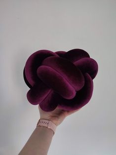 a hand is holding up a purple object in the shape of a flower on a white background