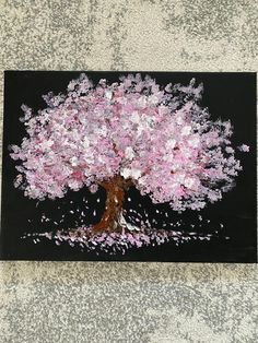 a painting of a tree with pink and white flowers on black paper, sitting on the ground