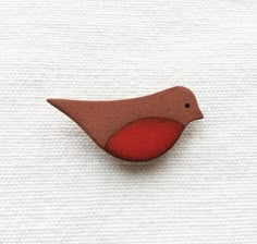 a red bird brooch sitting on top of a white cloth covered floor next to a piece of wood