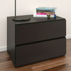 a black night stand with two books on top and a lamp next to it in front of a white wall