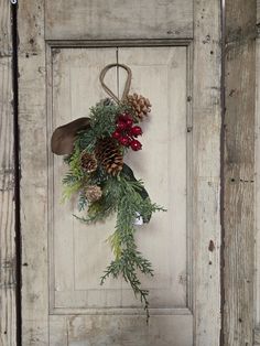 a wreath with pine cones and berries hangs on a door handle in an old wooden frame