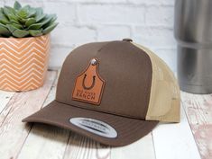 These popular personalized retro trucker hats are Yupoong 5 panel snapback hats. Custom hats with your brand  engraved on a leatherette cattle tag  will make a statement and look professional. Our Leatherette patches offer the look and feel of genuine leather without using animal products. These richly textured, water resistant patches ensure you will get the quality you expect and are rugged enough to stand up to any adventure. Our patches are adhered to your cap using a industrial hat press to Western Brown Trucker Hat With Flat Bill, Western Style Brown Trucker Hat With Flat Bill, Western Style Brown Flat Bill Baseball Cap, Brown Western Trucker Hat With Flat Brim, Western Brown Snapback Hat With Flat Bill, Adjustable Brown Trucker Baseball Cap, Brown Adjustable Trucker Baseball Cap, Brown Trucker Snapback Hat, Adjustable Brown Trucker Hat