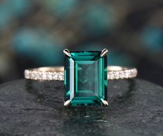 an emerald and diamond ring sitting on top of a rock