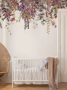 a baby crib in front of a wall with flowers hanging from it's side