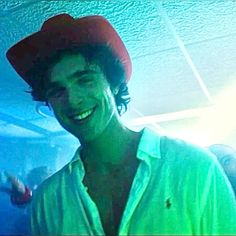 a young man wearing a red hat and green shirt smiles at the camera while standing in a room