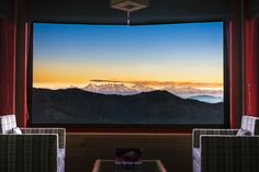 two chairs and a table in front of a large window with the view of mountains