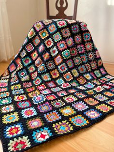 a black crocheted blanket sitting on top of a wooden floor next to a chair