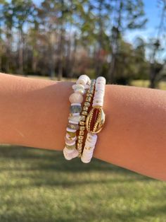 a woman's arm with three bracelets on it and trees in the background