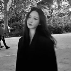 a woman with long hair standing in front of some trees and bushes at night time