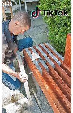 a man kneeling down on the ground working on a wooden bench with a hammer in his hand