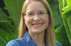 a woman wearing glasses standing in front of some green plants and smiling at the camera