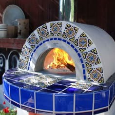 an outdoor pizza oven with blue and white tiles on the outside, in front of a potted plant