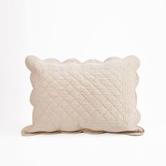 a white quilted pillow with scalloped edges on a white background in the shape of a rectangle