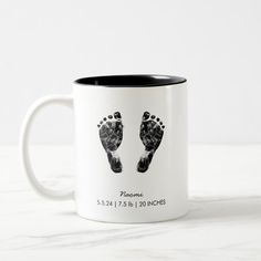 two black and white coffee mugs with the imprint of someone's feet on them