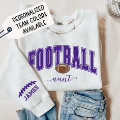 a white shirt with purple football on it next to some blue jeans and a fan