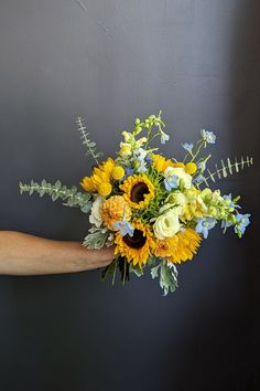 a person holding a bouquet of sunflowers and greenery in their left hand