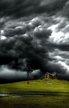 a house in the middle of a green field under a cloudy sky with dark clouds