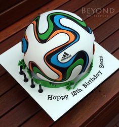 a soccer ball cake sitting on top of a wooden table next to a white card