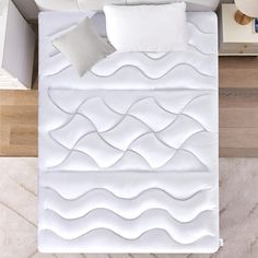 an overhead view of a bed with white sheets and pillows on it, next to a night stand