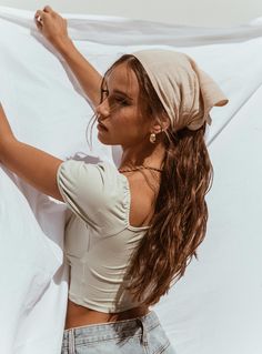 a woman with long brown hair wearing a white shirt and jeans is leaning against a wall