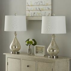 two lamps are sitting on top of a dresser in front of a painting and flowers