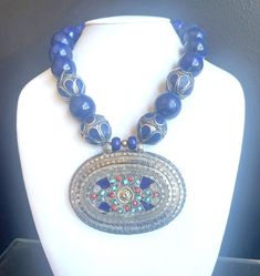 "20mm blue lapis round beads, 20mm Afghan Turkman Alpaca metal wrapped design beads, Uzbek Alpaca pendant with lapis, coral and silver (3'W x 2.5\"H), silver hook clasp. 20\"OA" Blue Lapis Lazuli Jewelry With Large Beads, Blue Lapis Lazuli Necklace With Large Beads, Artisan Lapis Lazuli Jewelry With Polished Beads, Traditional Gemstone Beaded Round Pendant, Traditional Blue Oval Beads Jewelry, Traditional Jewelry With Round Lapis Lazuli Beads, Lapis Lazuli Beaded Necklaces With Large Beads As Gift, Traditional Round Pendant Jewelry With Gemstone Beads, Lapis Lazuli Beaded Necklace With Large Beads For Gift