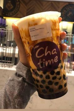 a person holding up a cup with cheesy toppings on it in front of a building