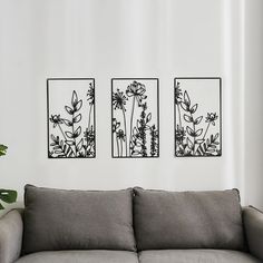 three black and white paintings on the wall above a gray couch in a living room