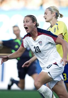 two female soccer players in action on the field, one is holding her hand out