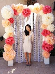 a woman standing in front of a white and orange flower arch