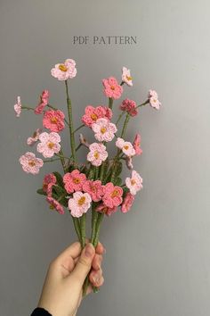 a hand holding up a bunch of pink crocheted flowers against a gray wall