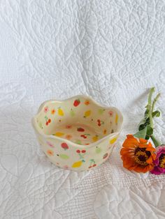 two flowers sitting next to each other on a white bed sheet with a flower vase in the foreground