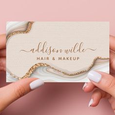 two hands holding up a business card with gold foil on the front and bottom, against a pink background