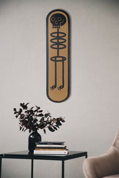 a table with a vase on it next to a chair and a wall hanging above it