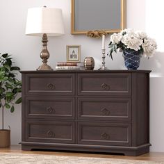 a brown dresser with flowers on top and a mirror above it in a living room