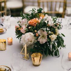 an arrangement of flowers and candles on a white table cloth with gold numbers for the number four