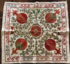 an embroidered table cloth with red and green designs on white fabric, sitting on a wooden surface