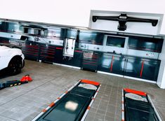 a white sports car parked in a garage with tools on the floor and cabinets behind it