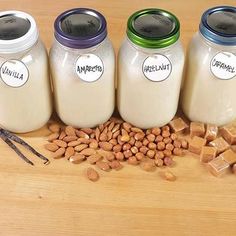 four jars filled with milk and nuts on top of a wooden table