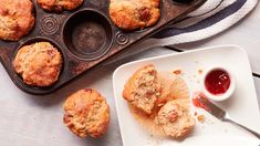 muffins in a muffin tin with jam on the side next to it