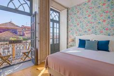 a bed sitting next to a window in a room with flowers on the wall and wooden floors