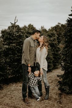 a man and woman kissing while standing in front of christmas trees