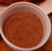 a cup filled with cinnamon sitting on top of a wooden table next to a piece of bread