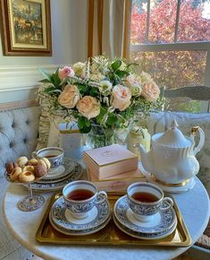 there is a tray with tea and books on it next to a vase filled with flowers