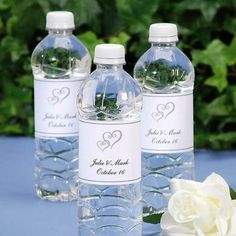 three water bottles with labels on them sitting next to a white rose