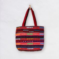 The Akha-Ani large tote bag is the perfect everyday cotton carry-all. It's generous size is designed to hold all the essentials or a lot...! The decoration on the exterior of the bag is hand crafted by the Akha people who live in the hills of  Myanmar. The pattern is colourful and embroidered with different coloured fabrics and threads. *  Bag 46cm Wide x 40cm Depth *  27cm handles *  Inside Bag large open pocket 21cm X 21cm *  Inside zippered pocket 21cm X 21cm *  Also Drawstring compartment in middle of bag *  Cotton with woollen and cotton embroidery *  Padded Base *  Select from a range of woven colour variations Care: Dry Clean only Made in Burma | Fair Trade Disclaimer: Mingalaba products are all made by individual artisans. Each Bag is unique and it's very rare we see 2 perfectly id Red Square Canvas Bag For Daily Use, Red Double Handle Beach Bag For Everyday Use, Red Large Capacity Canvas Tote Bag, Large Capacity Red Canvas Tote Bag, Red Cotton Double Handle Shoulder Bag, Red Double Handle Beach Bag, Red Double Handle Cotton Shoulder Bag, Traditional Tote Beach Bag For Everyday Use, Traditional Tote Beach Bag