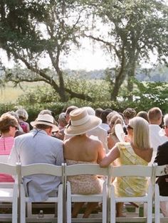 a group of people sitting on top of white chairs in front of a tree filled field