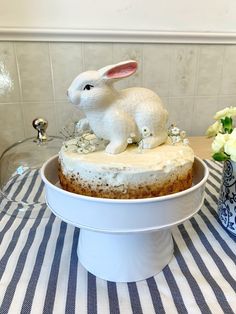 a cake with white frosting and a rabbit figurine on top sits on a table