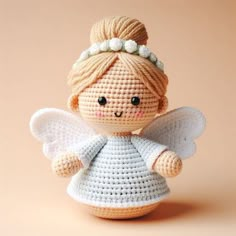 a small crocheted angel doll sitting on top of a table next to a pink wall