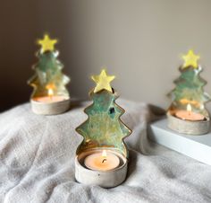 three small christmas trees sitting on top of a bed next to a lit candle holder